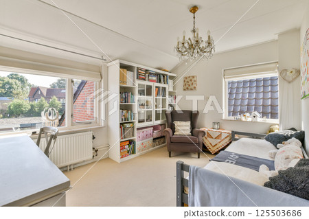 A bright and inviting reading area featuring a comfortable chair, bookshelves filled with books, and soft decor. Perfect for relaxing with a good book. 125503686