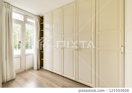 Spacious interior featuring white cabinets, natural light from windows, and a warm wooden floor, creating an inviting atmosphere for any room. 125503688