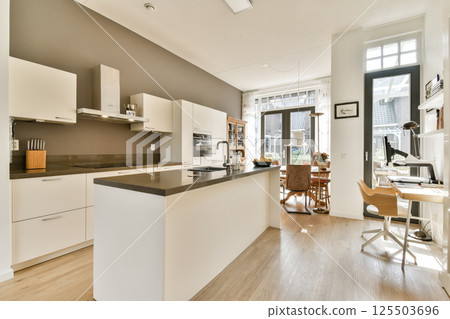 A sleek and modern kitchen featuring minimalist cabinetry, a large countertop, and a well-lit dining area that enhances the overall aesthetic. A sleek and modern kitchen featuring minimalist cabinetry, a large countertop, and a well-lit dining area that enhances the overall aesthetic. 125503696