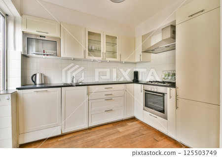 A stylish kitchen featuring white cabinets, black countertops, and modern appliances, emphasizing a clean and contemporary design. 125503749