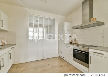 A sleek modern kitchen featuring white cabinetry, a glass door, and stainless steel appliances, creating a bright and spacious cooking space. 125503761