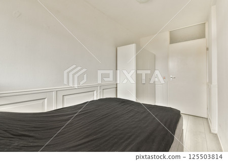 A simplistic and modern bedroom featuring a dark bedspread, light walls, and a closet. The room exudes tranquility and minimalism with clean lines. A simplistic and modern bedroom featuring a dark bedspread, light walls, and a closet. The room exudes tranquility and minimalism with clean lines. 125503814