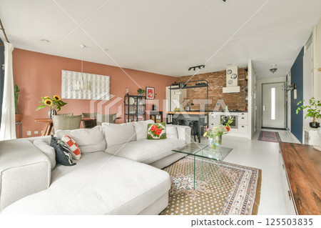 A chic modern living room featuring a comfortable sofa, vibrant decor, and an open kitchen design, creating a warm and inviting atmosphere for relaxation. 125503835