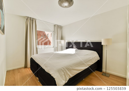 A sleek modern bedroom featuring a light color scheme, large window for natural light, and minimalist decor emphasizing comfort and simplicity. A sleek modern bedroom featuring a light color scheme, large window for natural light, and minimalist decor emphasizing comfort and simplicity. 125503839