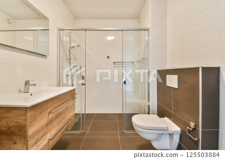 A stylish and contemporary bathroom featuring a glass shower, wooden vanity, and sleek fixtures, showcasing functionality and elegance. 125503884