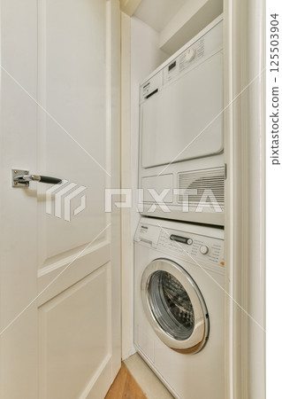 A neatly organized laundry area featuring a stacked washer and dryer tucked away in a built-in closet. The clean lines and bright color create a functional space. 125503904