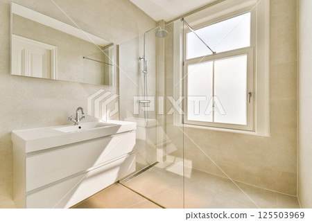 A stylish modern bathroom featuring a sleek shower and a well-placed mirror. Natural light streams through the window, enhancing the minimalist aesthetic. A stylish modern bathroom featuring a sleek shower and a well-placed mirror. Natural light streams through the window, enhancing the minimalist aesthetic. 125503969