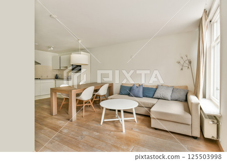 This stylish living room features a contemporary design with light wood flooring, a cozy sofa, and dining area, all in a spacious, bright setting. 125503998