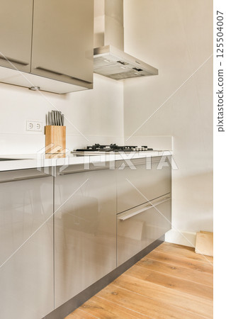 Sleek modern kitchen showcasing minimalistic cabinetry, a countertop, and a neatly organized cooking area with essential utensils. 125504007