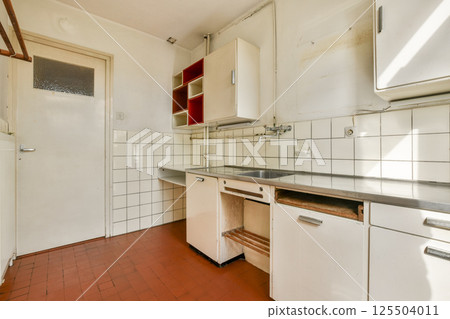 A clean and simple kitchen featuring white tiles and minimalist cabinetry. The warm tones create a cozy atmosphere, perfect for cooking. 125504011