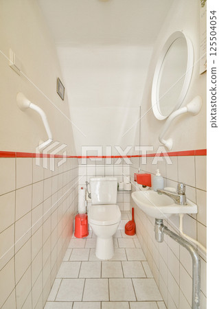 A compact modern bathroom featuring a white toilet, sink, and minimalistic design elements enhanced by a red accent stripe. A compact modern bathroom featuring a white toilet, sink, and minimalistic design elements enhanced by a red accent stripe. 125504054