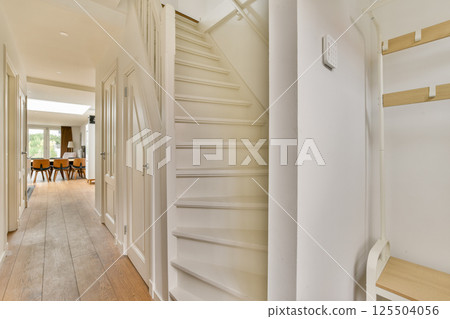 A spacious interior view showcasing a modern hallway leading to a staircase, illuminated by natural light, complementing contemporary design elements. 125504056