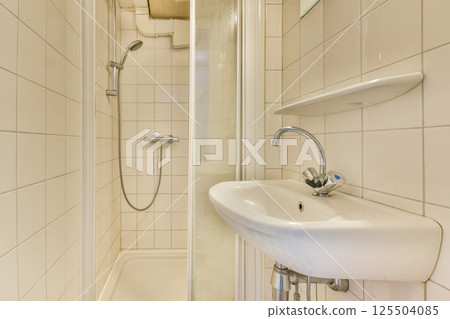 A sleek and minimalistic bathroom designed featuring a spacious shower enclosure and a stylish sink. The tiles enhance the contemporary aesthetic. 125504085