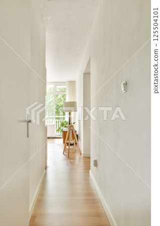 A bright and airy interior hallway featuring a minimalist design with wooden flooring and a modern lamp, inviting natural light from large windows. A bright and airy interior hallway featuring a minimalist design with wooden flooring and a modern lamp, inviting natural light from large windows. 125504101