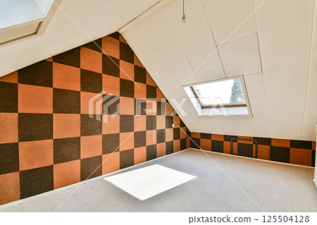 An inviting attic space featuring bold checker-patterned walls and generous natural light from a skylight. The room is ready for further decoration and use. An inviting attic space featuring bold checker-patterned walls and generous natural light from a skylight. The room is ready for further decoration and use. 125504128