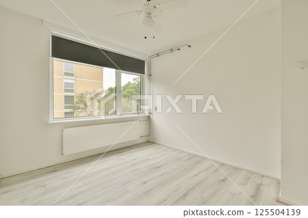 A minimalist interior featuring white walls and flooring, with a large window allowing natural light. The space is simple yet inviting, suitable for various decor styles. A minimalist interior featuring white walls and flooring, with a large window allowing natural light. The space is simple yet inviting, suitable for various decor styles. 125504139