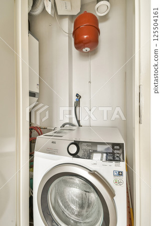 A clean and organized laundry room featuring a washing machine, with plumbing visible and a fire extinguisher hanging on the wall. Ideal for practical home designs. 125504161