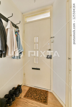 An inviting entryway showcasing a door, a coat rack with jackets, and shoes on a wooden floor, perfect for welcoming guests in a home. 125504164