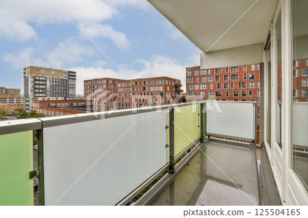 A contemporary balcony of an apartment complex showcases a vibrant cityscape with modern buildings against a clear blue sky, creating a serene urban atmosphere. 125504165