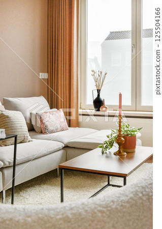 A beautifully designed modern living room featuring soft tones, elegant decor, and natural light filtering through large windows, creating a warm atmosphere. 125504166