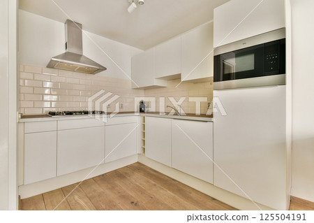 A sleek modern kitchen featuring white cabinetry, clean lines, and a minimalist aesthetic. Designed for functionality and elegance with contemporary appliances. 125504191