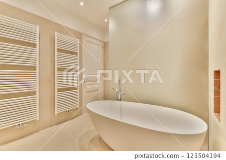 A sleek and contemporary bathroom featuring a freestanding bathtub, clean lines, and a stylish radiator. The warm tones create a serene atmosphere. 125504194