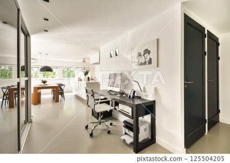 A sleek and contemporary home office featuring a desk, ergonomic chair, and stylish decor set in a bright, open space with natural lighting. 125504205
