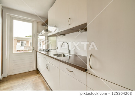 Sleek modern kitchen features minimalist cabinetry, a gas stove, and large windows offering natural light, enhancing the contemporary aesthetic. 125504208