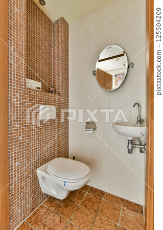 A stylish modern bathroom featuring elegant tiles, a round mirror, and minimalist fixtures. The design emphasizes cleanliness and contemporary aesthetics. 125504209