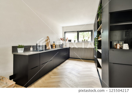 A sleek and stylish modern kitchen featuring dark cabinetry, vibrant plants, and a spacious design that enhances functionality and aesthetics. 125504217