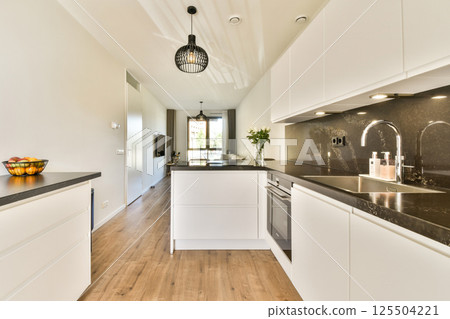 Stylish kitchen featuring contemporary design with white cabinets, sleek countertops, and natural lighting, creating a bright and inviting atmosphere. 125504221