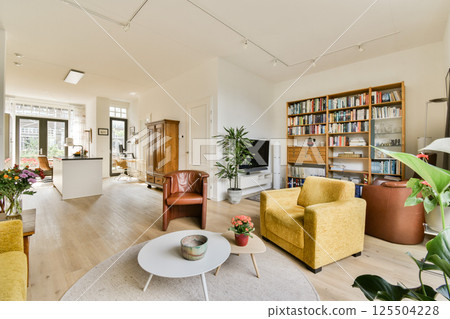 Spacious living room featuring bright furniture, bookshelves, and natural lighting, creating a warm and inviting atmosphere perfect for relaxation. Spacious living room featuring bright furniture, bookshelves, and natural lighting, creating a warm and inviting atmosphere perfect for relaxation. 125504228