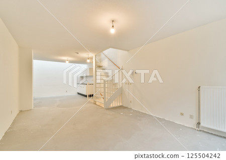 An empty modern interior featuring white walls, a staircase, and overhead lighting. The space offers a clean, minimalist design ideal for various purposes. An empty modern interior featuring white walls, a staircase, and overhead lighting. The space offers a clean, minimalist design ideal for various purposes. 125504242