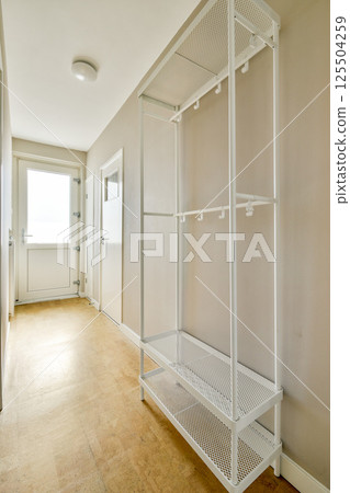 A spacious and well-lit hallway featuring a sleek metal shelving unit and light-colored walls, showcasing minimalist interior design aesthetics. 125504259