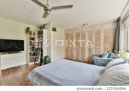 A serene bedroom featuring a stylish design, warm wooden flooring, and natural light streaming through large windows, creating a relaxing atmosphere. 125504264