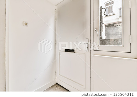 the inside of a room with white walls and wooden floors, including a door that leads to a small window 125504311