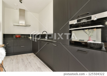 A sleek, modern kitchen design featuring dark cabinets, a minimalist layout, and a touch of elegance with stainless steel appliances. Ideal for contemporary living. 125504322