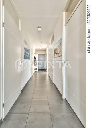 A sleek and well-lit corridor featuring multiple doors, tiled flooring, and contemporary artwork on the walls. Ideal for architectural insights and interior design inspiration. 125504335