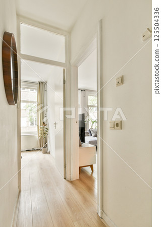 A spacious interior hallway featuring clean lines, a wooden floor, and natural light streaming through large windows. Minimalist design enhances the open feel. 125504336