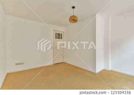 A clean, minimalist interior featuring neutral tones, a simple light fixture, and a door, providing a spacious and uncluttered ambiance. 125504338