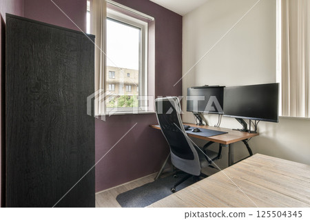 A sleek home office featuring a large window, a desk with a computer, and minimalist decor. Natural light enhances the workspace ambiance for productivity. 125504345