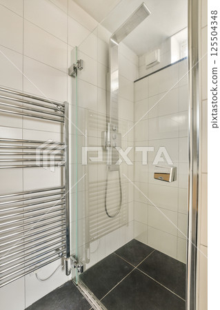 A sleek and modern shower room featuring a glass enclosure, chrome fixtures, and contemporary tiles, creating a minimalist aesthetic. 125504348