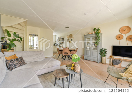 A bright and modern living room featuring a cozy sofa, stylish decor, and abundant greenery, creating a welcoming and serene atmosphere. 125504353