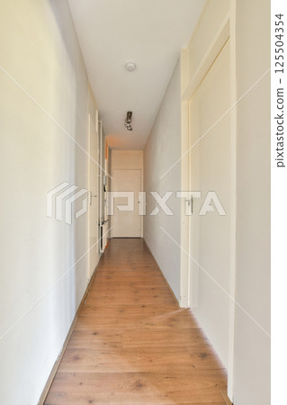 A clean and simple corridor showcasing a light-colored wall and wooden floor, leading to a closed door, creating a sense of openness and tranquility. 125504354