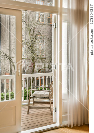 A modern balcony featuring a wooden floor and large windows that offer a view of trees and an inviting outdoor space for relaxation. 125504357
