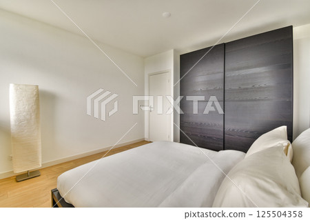 A modern bedroom showcasing a minimalist design with a stylish bed, elegant lamp, and sleek wardrobe. The neutral tones enhance the serene atmosphere. A modern bedroom showcasing a minimalist design with a stylish bed, elegant lamp, and sleek wardrobe. The neutral tones enhance the serene atmosphere. 125504358