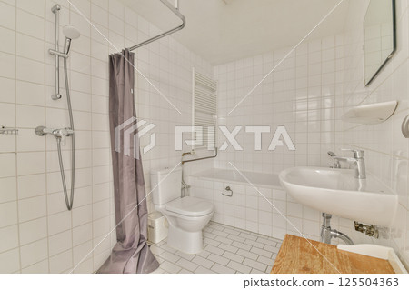 A stylish bathroom featuring white tiled walls, a shower area with a curtain, a sink, and wooden accents, blending functionality with modern design. 125504363