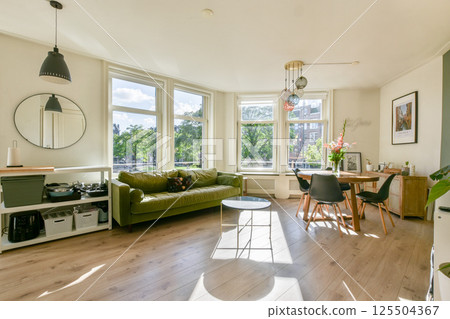 A spacious living room featuring large windows that allow natural light, a comfortable green sofa, and stylish decor elements that enhance the inviting atmosphere. A spacious living room featuring large windows that allow natural light, a comfortable green sofa, and stylish decor elements that enhance the inviting atmosphere. 125504367
