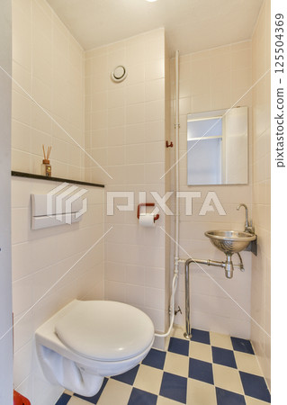 A clean and minimalistic bathroom featuring a white toilet, blue checkered floor, and sleek fixtures. The walls are lined with simple tiles, providing a contemporary look. A clean and minimalistic bathroom featuring a white toilet, blue checkered floor, and sleek fixtures. The walls are lined with simple tiles, providing a contemporary look. 125504369