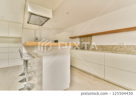 A sleek and modern kitchen featuring minimalist cabinetry, an elegant countertop, and stylish bar stools. The space embodies contemporary design principles. 125504430